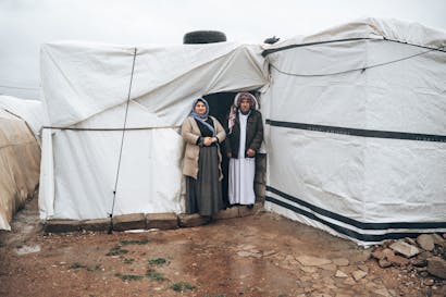 oudere vrouw en man staan voor hun witte tent in vluchtelingenkamp in noord-irak
