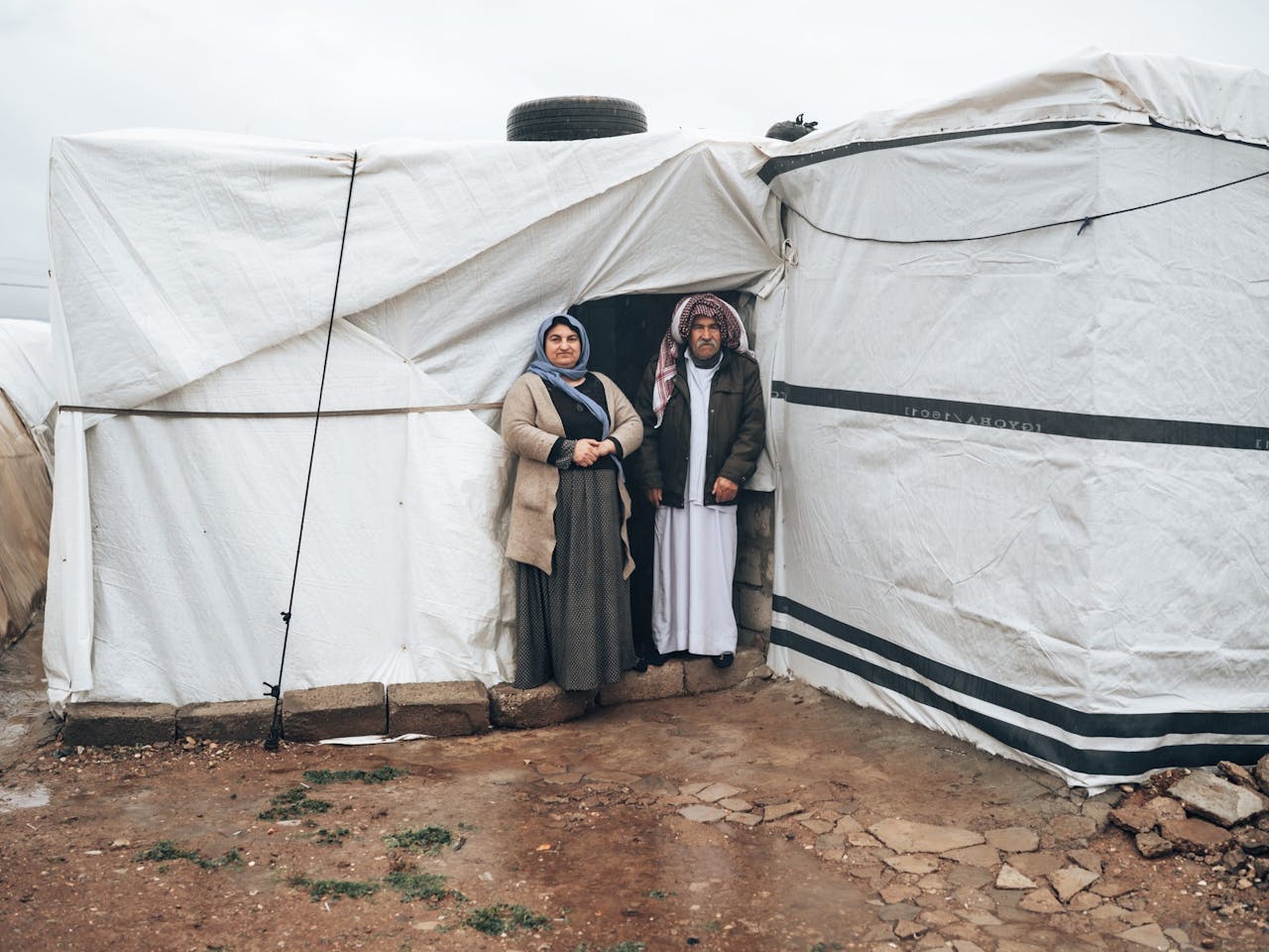 oudere vrouw en man staan voor hun witte tent in vluchtelingenkamp in noord-irak