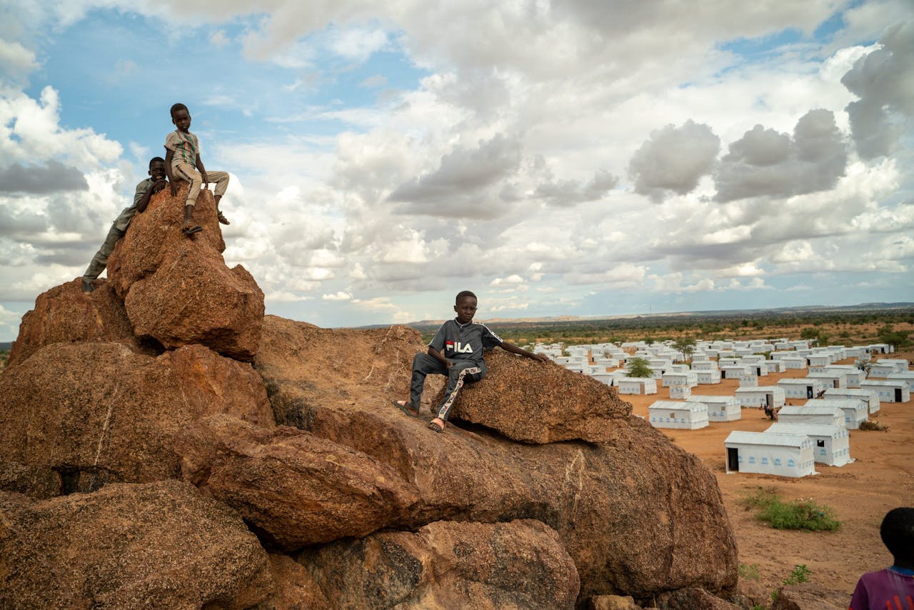 Drie jongetjes zitten voor een vluchtelingenkamp in Tsjaad