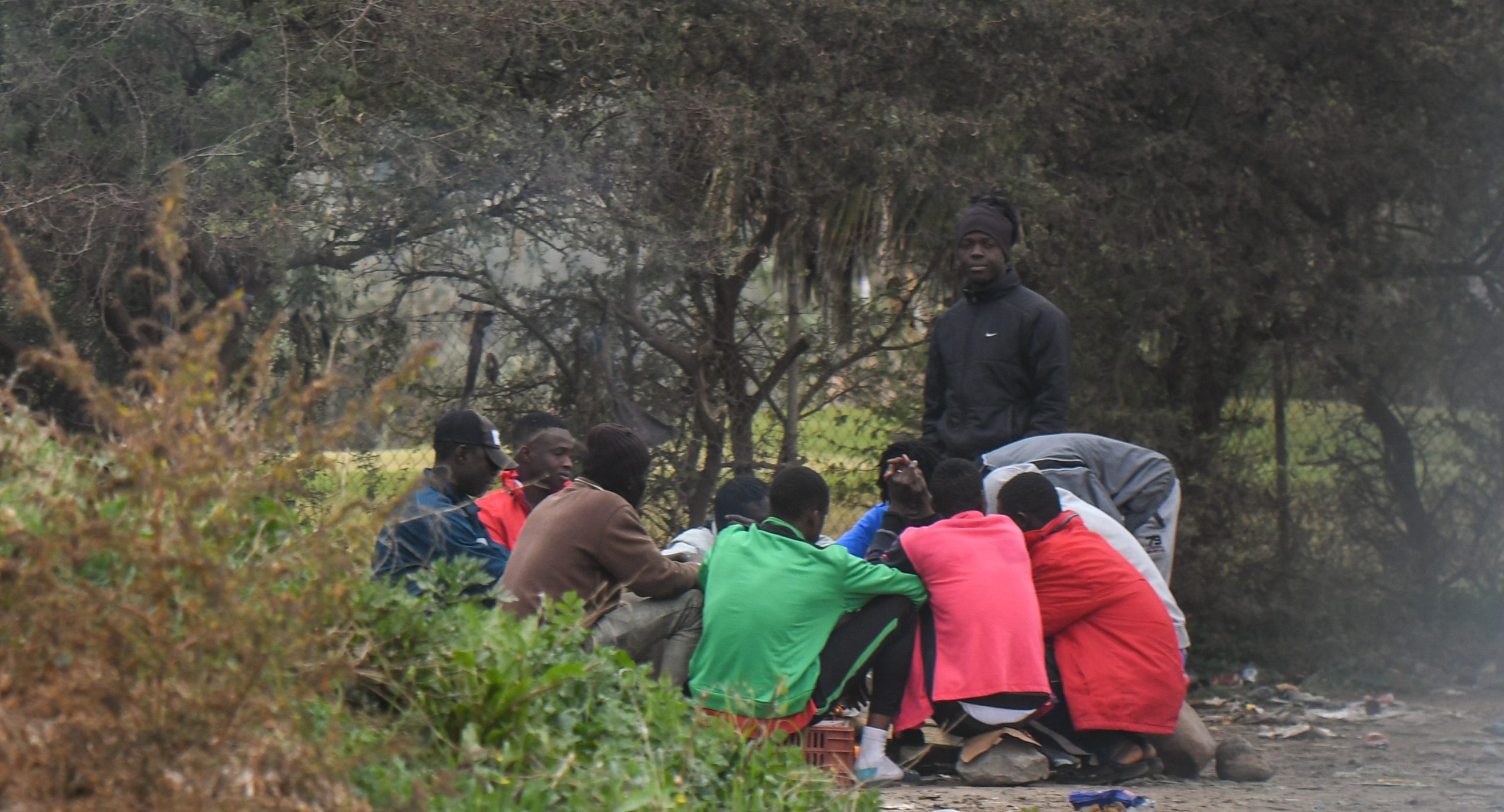 Een groep vluchtelingen zit naast het grenshek tussen Marokko en Spanje, in Melilla.