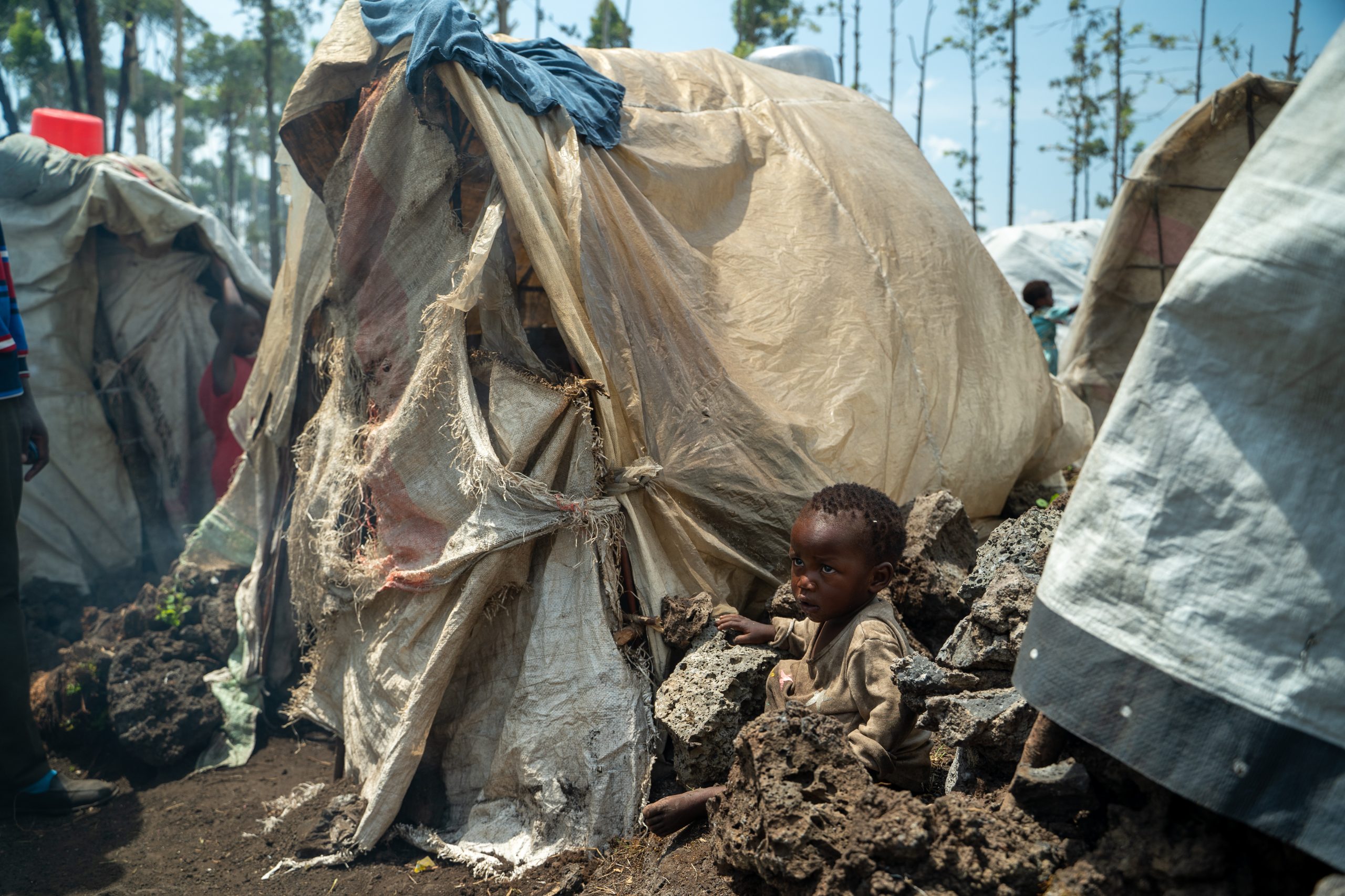een jongetje zit naast een tent in een vluchtelingenkamp bij Goma.