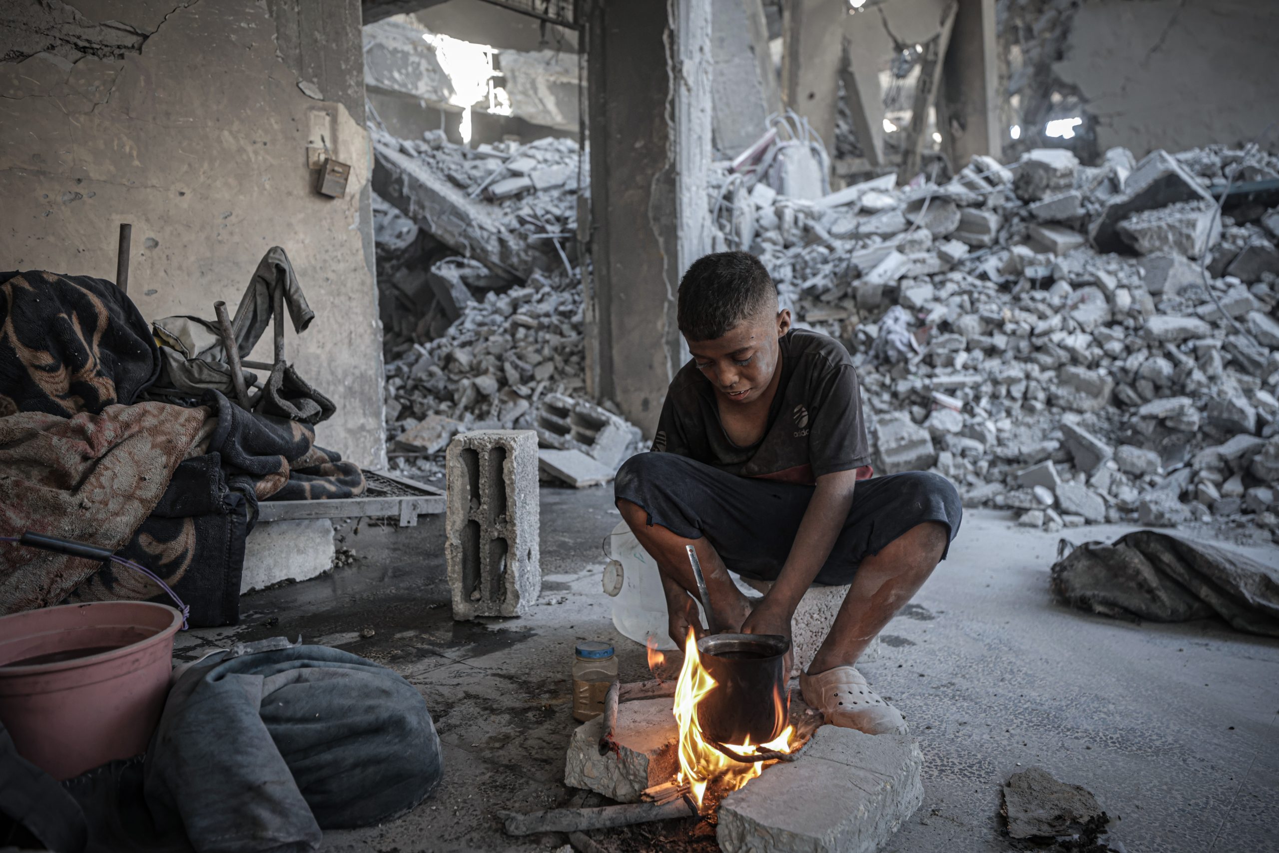 Een Palestijnse jongen maakt vuur in een verwoest gebouw in Gaza-Stad