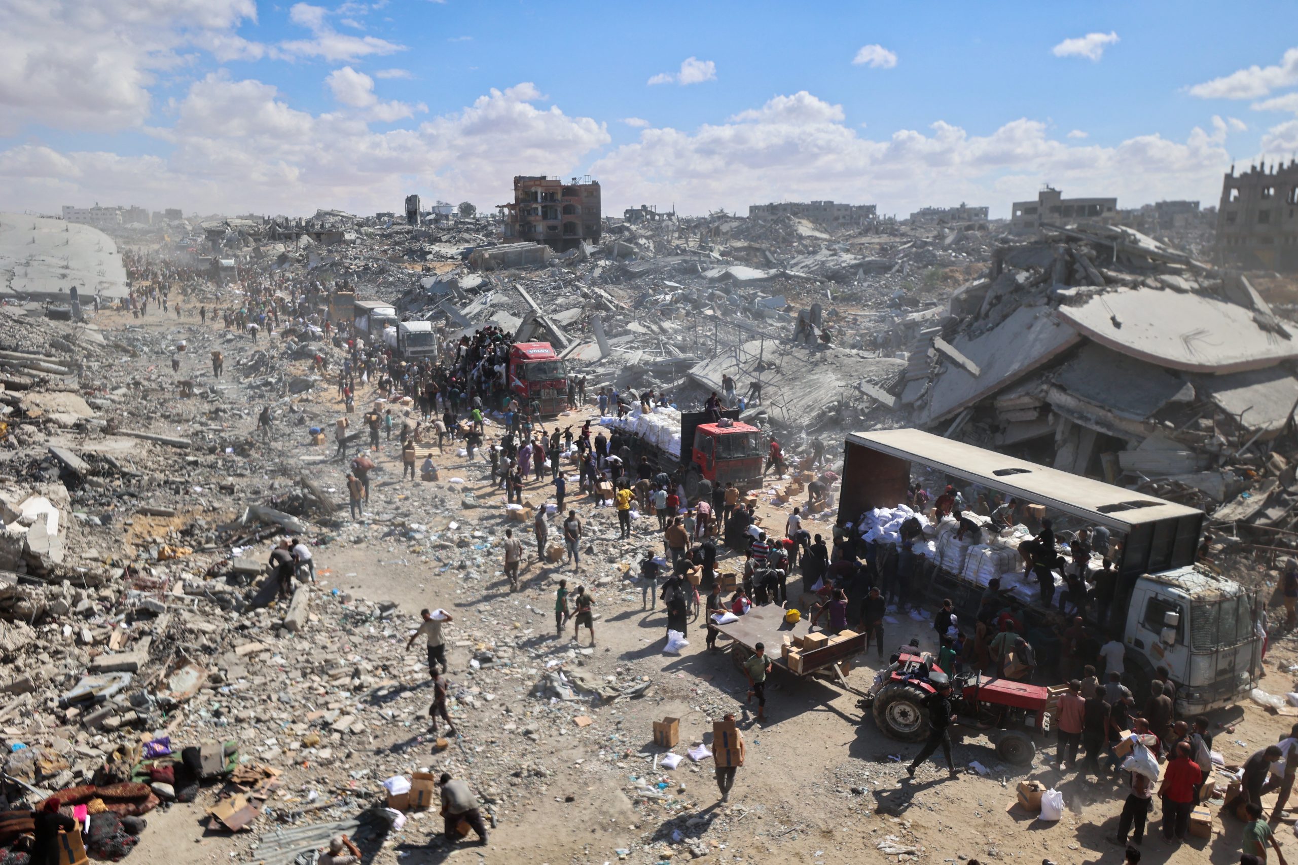 Palestijnen wachten bij een vrachtwagen met hulp die dankzij het staakt-het-vuren de grens weer over mag. Om de vrachtwagen heen is de verwoesting in Gaza te zien.