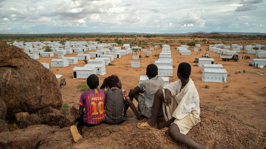 vier jongens zitten op een berg en kijken uit over een vluchtelingenkamp in Tsjaad
