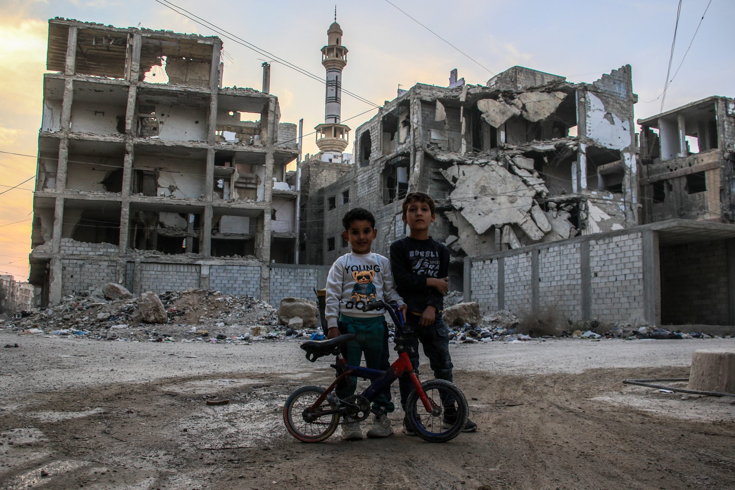 twee jongetjes staan met een fiets voor een verwoest gebouw in Damascus, Syrie
