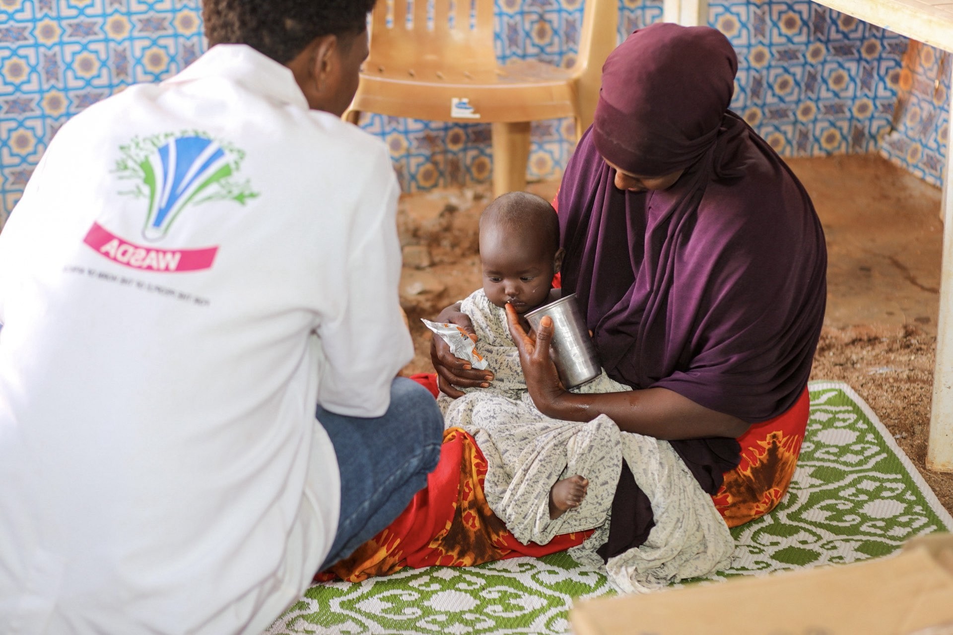 een klein jongetje dat bij zijn moeder op schoot zit krijgt voedsel van onze partner WASDA