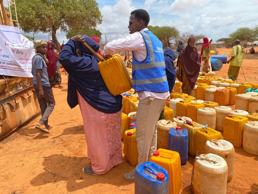 Een hulpverlener helpt een vrouw een jerrycan met schoon drinkwater op haar rug te hijsen.