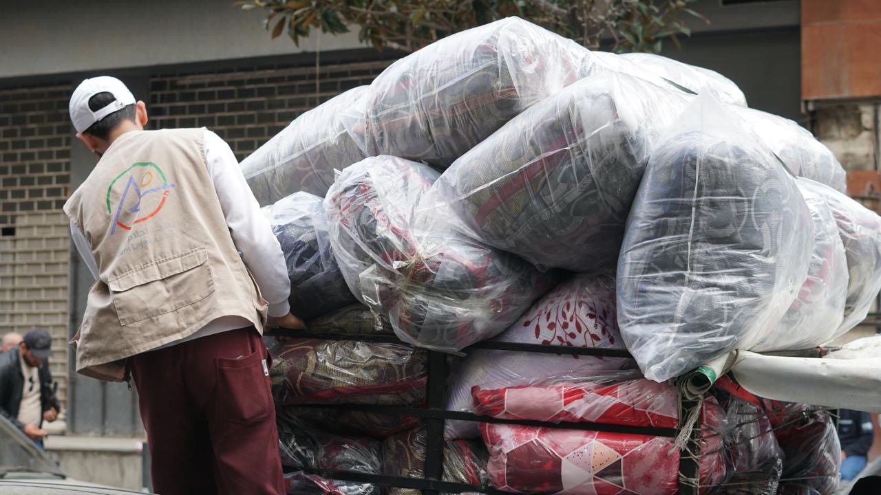 Een medewerker van onze partner Ahlam Lajea sjouwt kussens en dekens van een pallet in Beiroet