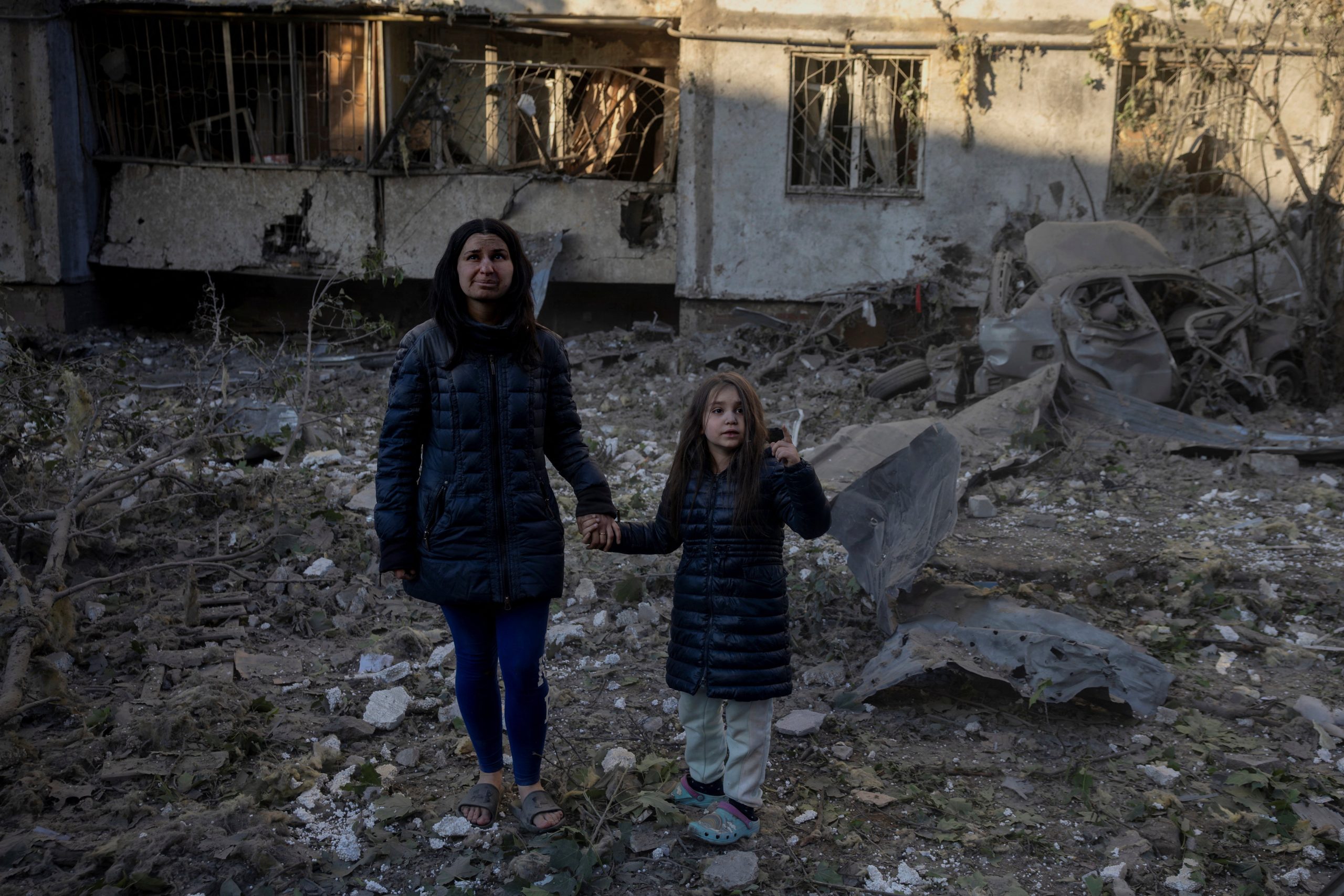 een moeder en dochter staan hand in hand voor een verwoest gebouw in Kyiv, Oekraine